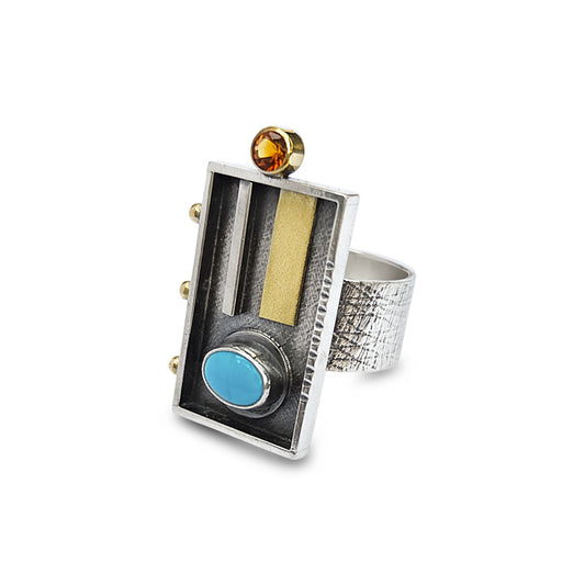 Silver ring with rectangular design featuring a blue gemstone, gold accent, and orange stone on a white background.