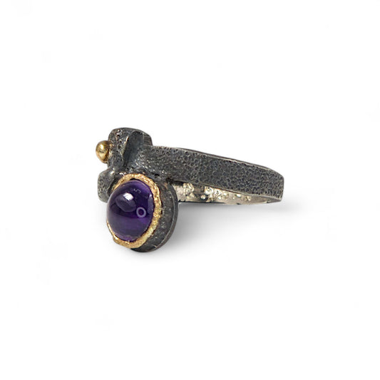 Ring with purple gemstone and gold accents on a white background