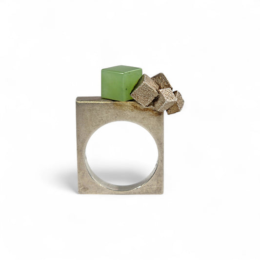 Silver ring with green cube and rock-like structure on a white background
